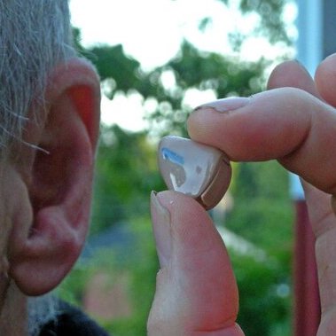 A man holding a hearing aid close to his ear